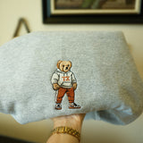 Gray sweatshirt with embroidered UT Austin bear design held by a person wearing a gold watch.