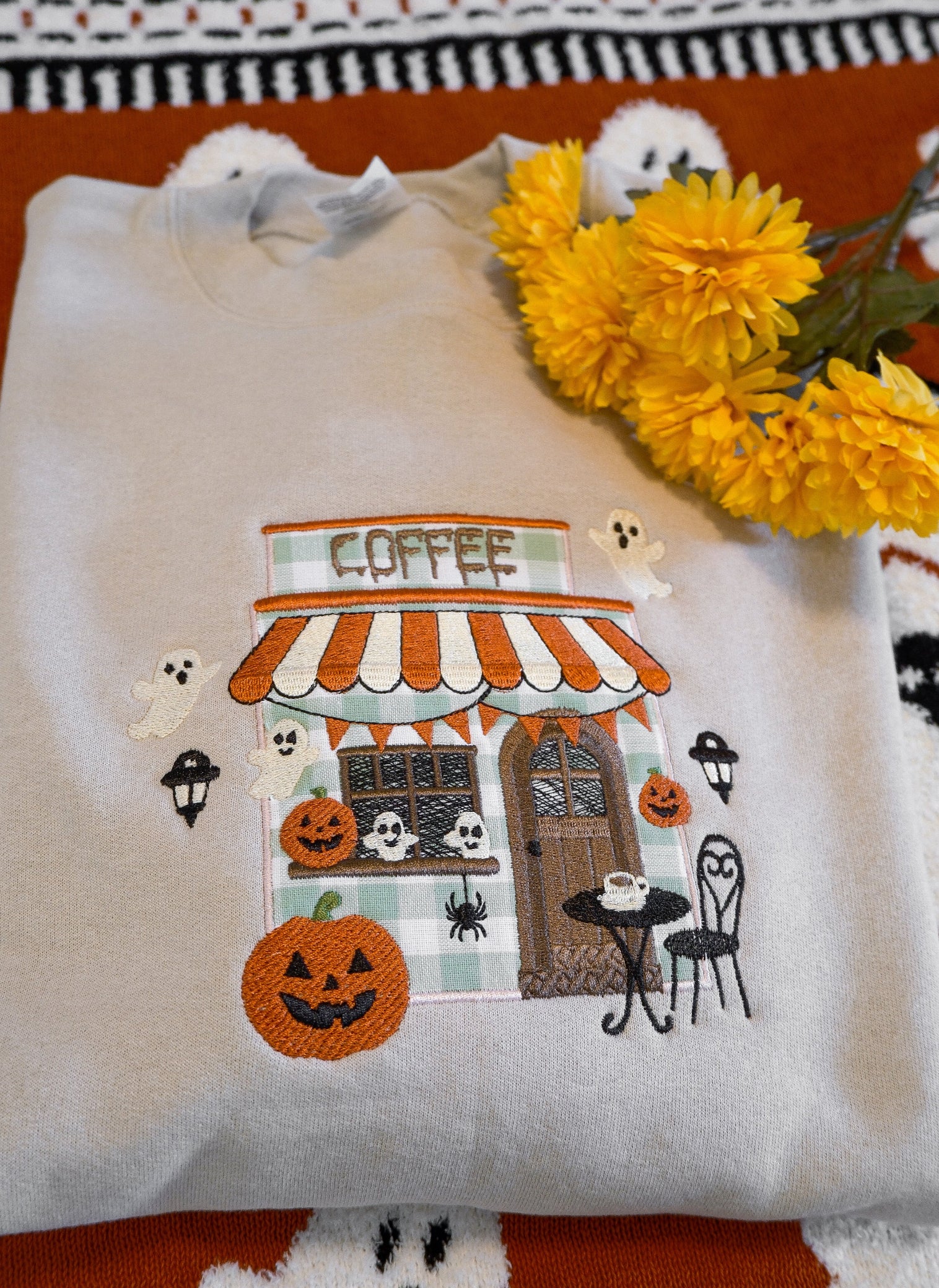 White shirt with Halloween-themed coffee shop design on a patterned surface with flowers.