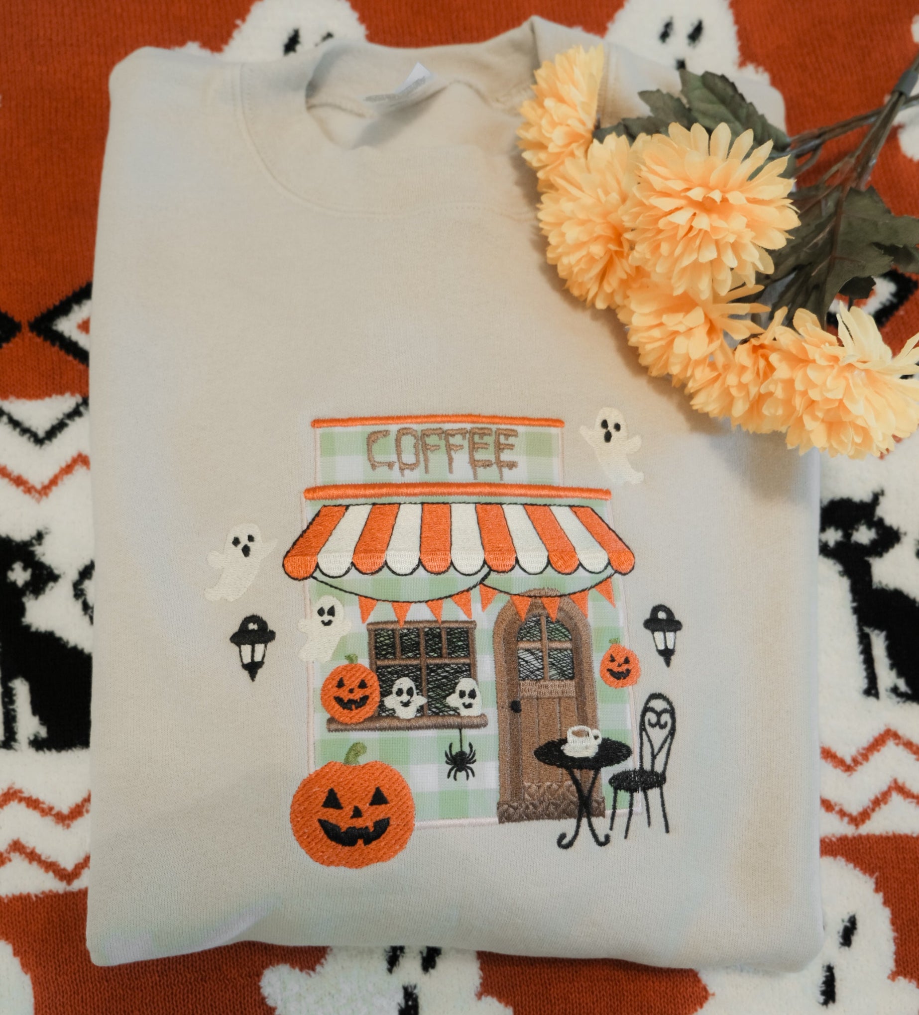 Folded embroidered sweatshirt with Halloween-themed design on a patterned fabric background