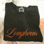 Burnt orange longhorns embroidered script on a black folded sweatshirt
