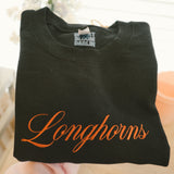 Burnt orange longhorns embroidered script on a black folded sweatshirt