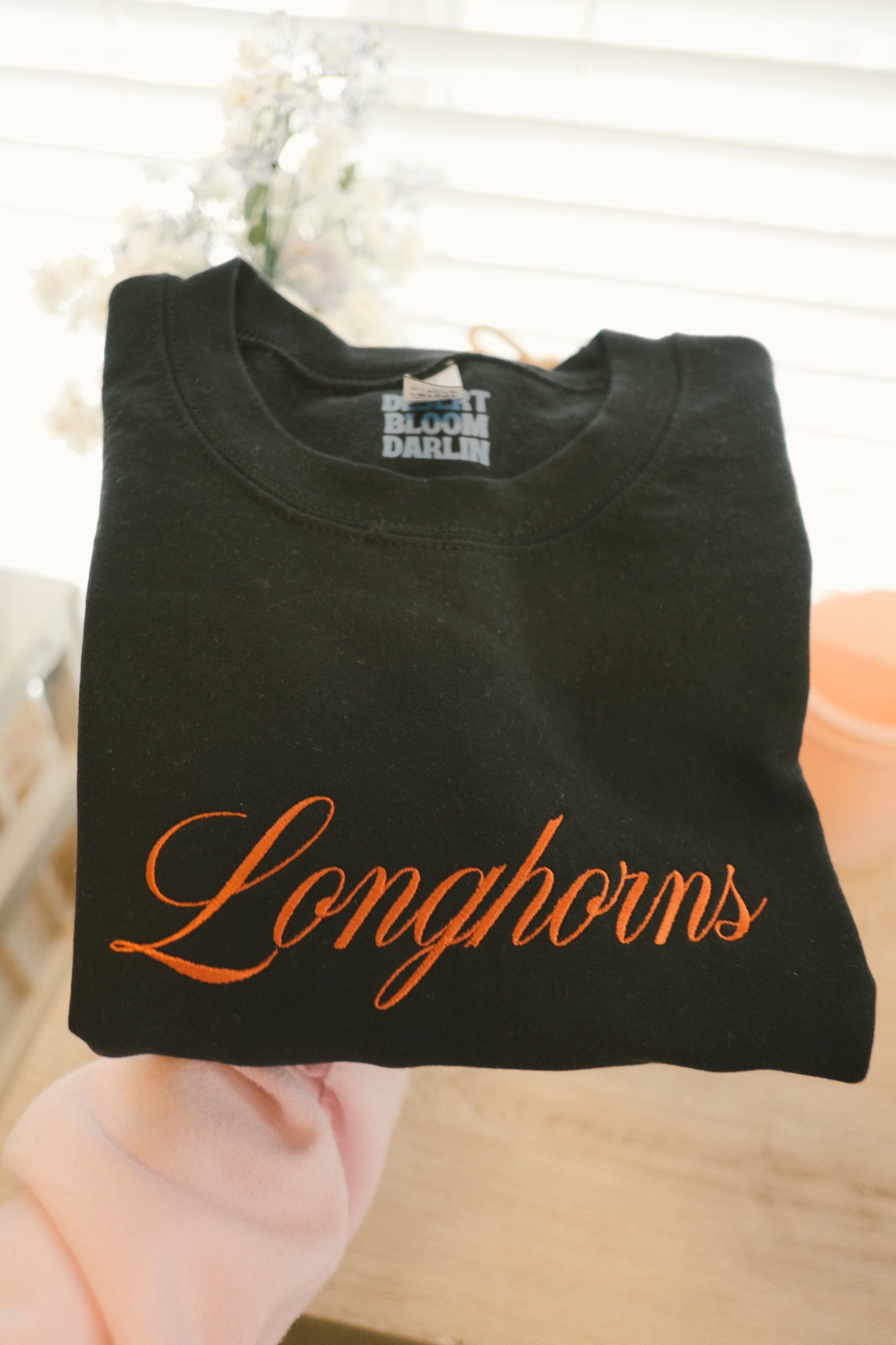 Burnt orange longhorns embroidered script on a black folded sweatshirt