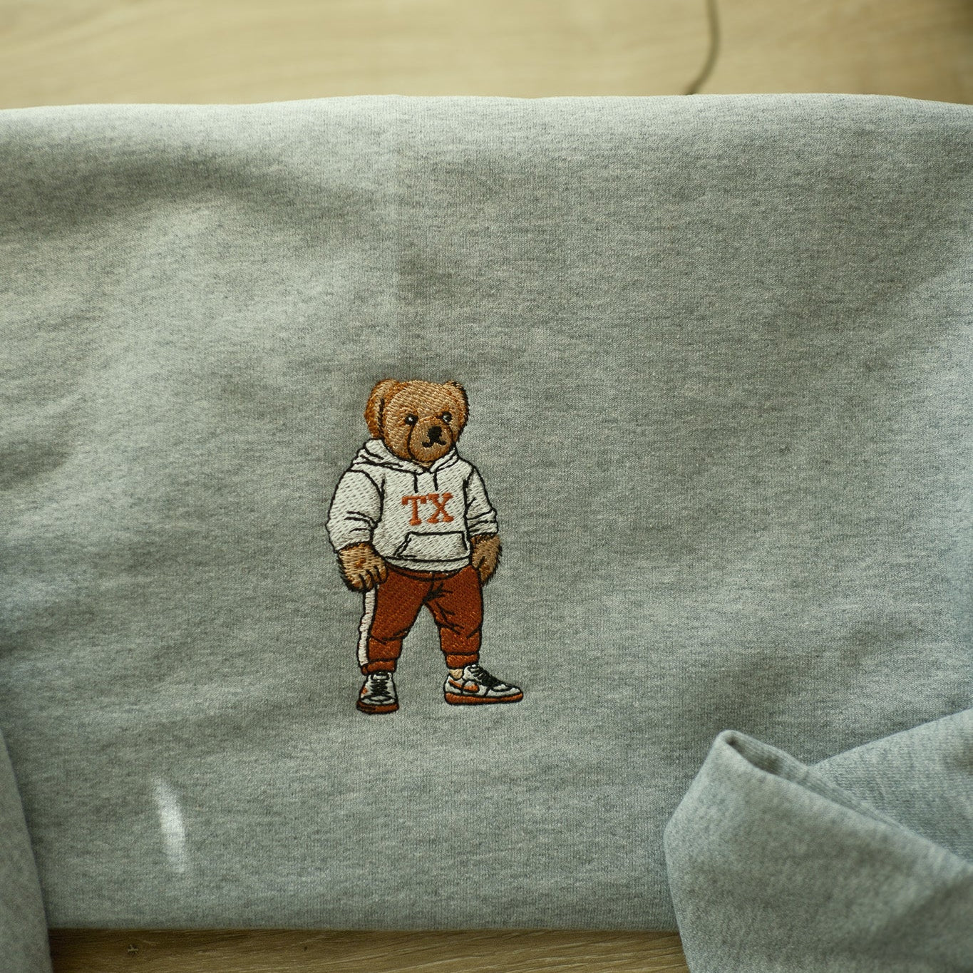 Gray sweatshirt with an embroidered bear design on a wooden surface