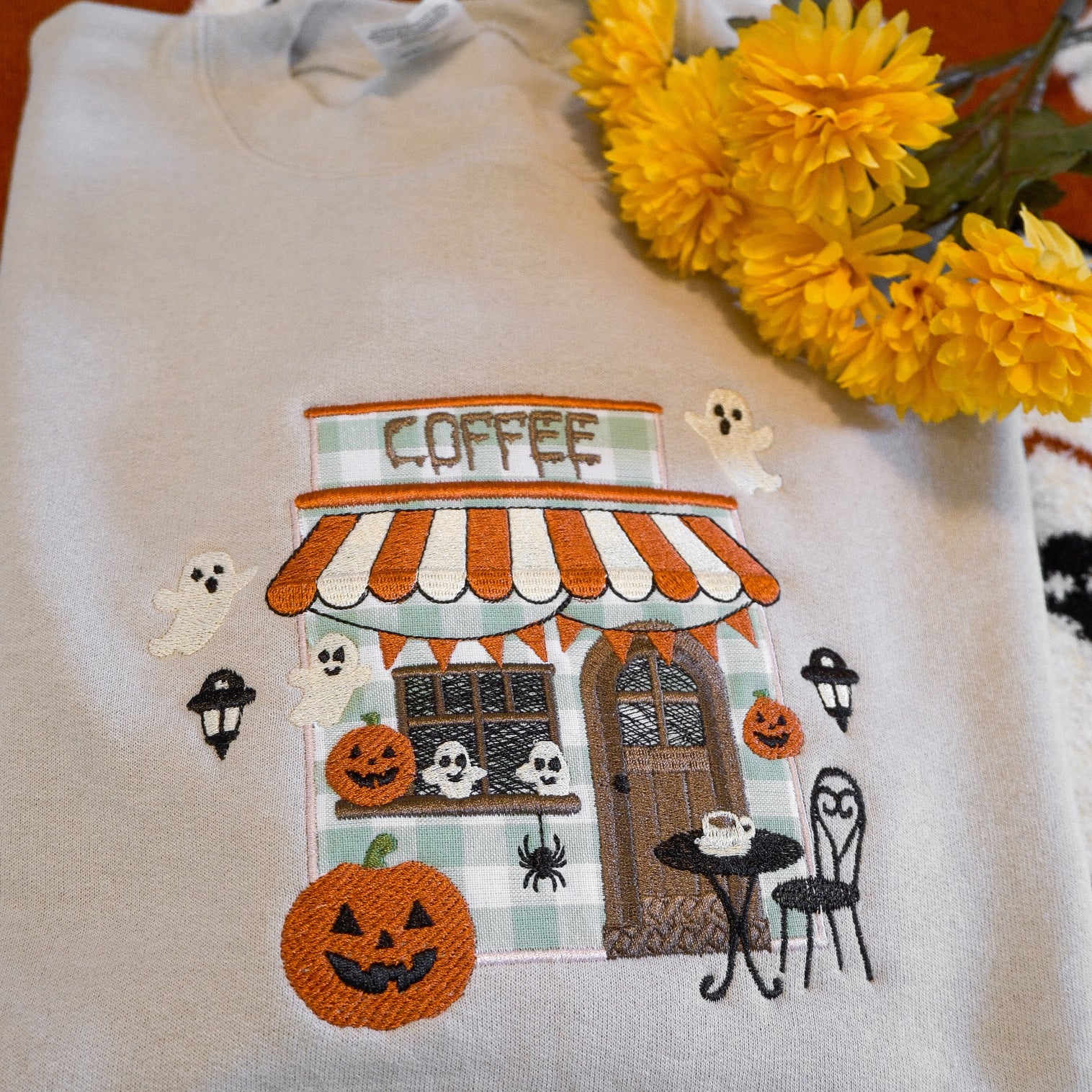 White shirt with Halloween-themed coffee shop design on a patterned surface with flowers.