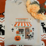 Folded embroidered sweatshirt with Halloween-themed design on a patterned fabric background