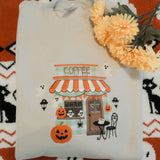 Folded embroidered sweatshirt with Halloween-themed design on a patterned fabric background