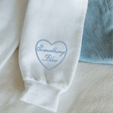 White garment with 'Something Blue' embroidery on a light background