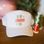 White cap with 'In My Longhorn Era' text on a wooden surface with spools of thread.