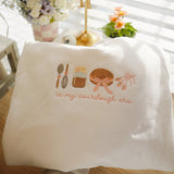 "White sweatshirt in embroidery hoop with 'In My Sourdough Era' design featuring a whisk, jar of starter, loaf of bread, and tied utensils in soft pink and brown tones.