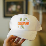 White cap with custom text held by a hand against a blurred indoor background